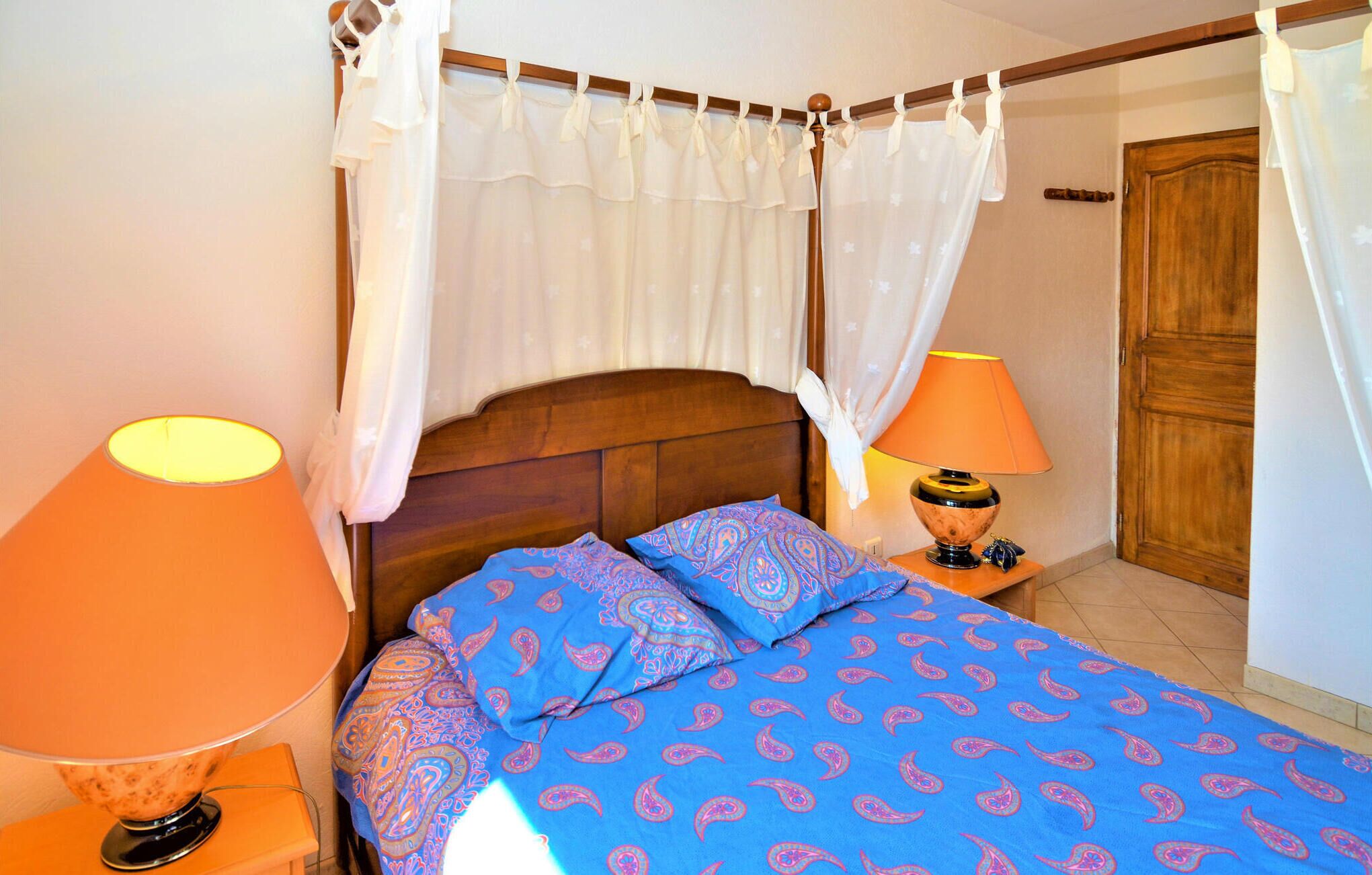 A bedroom with a wooden headboard, a canopy bed, two bedside lamps, and a patterned bedspread.