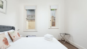 A bedroom with a bed, two windows, a radiator, and a chair. - Stunning Sydney Home 8 (Millers Point)