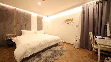 A modern bedroom with a large bed, a desk with a computer, and a small trash bin.
