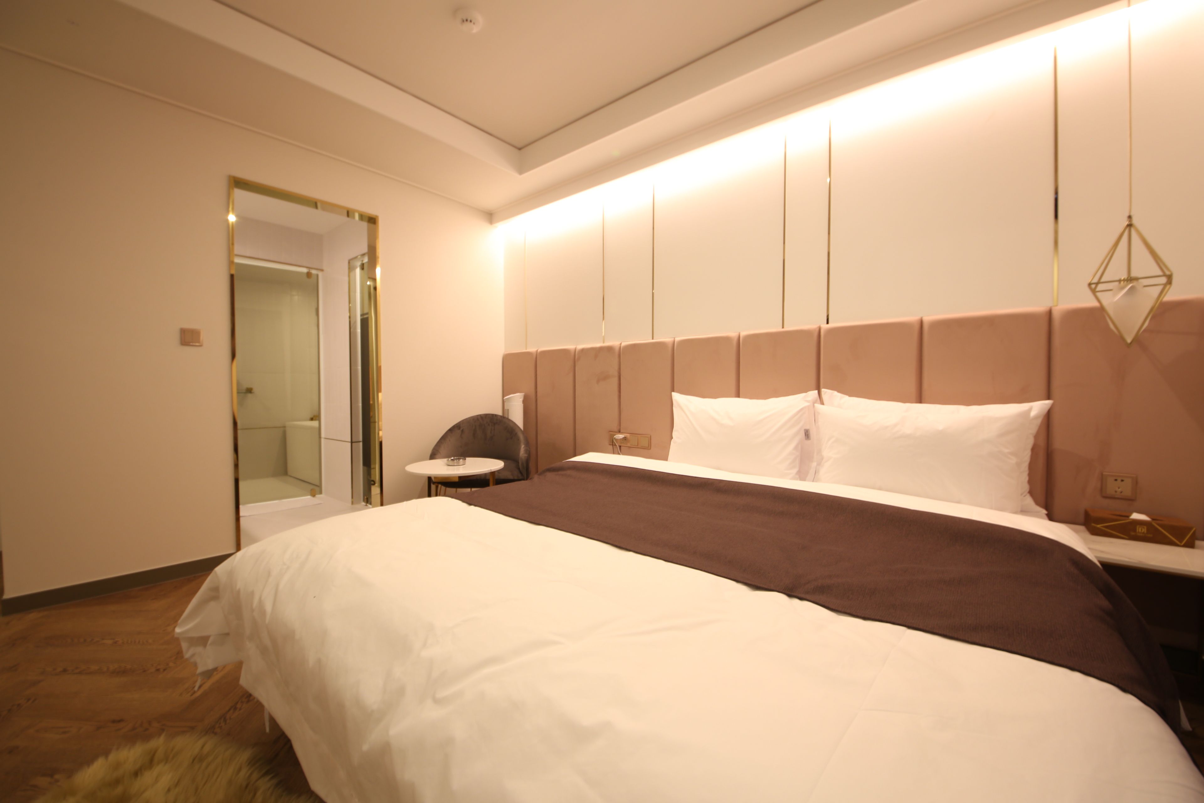 A hotel room with a large bed, a bedside table, a chair, and a mirror.