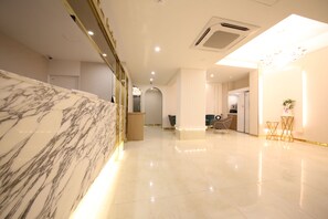 A modern hotel lobby with a marble reception desk, a seating area, and a clean, polished floor. - Den Basta Hotel (Busan)