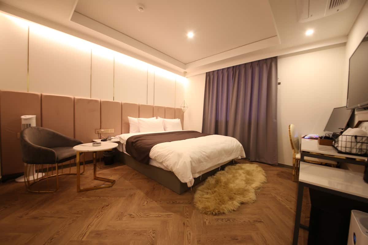 A modern hotel room with a bed, a desk, a chair, and a small table.