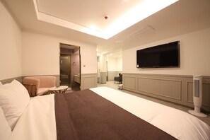 Habitación de hotel con una cama grande, televisión montada en la pared, una mesita y una silla.