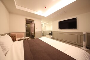 A hotel room with a large bed, a television mounted on the wall, a small table, and a chair.