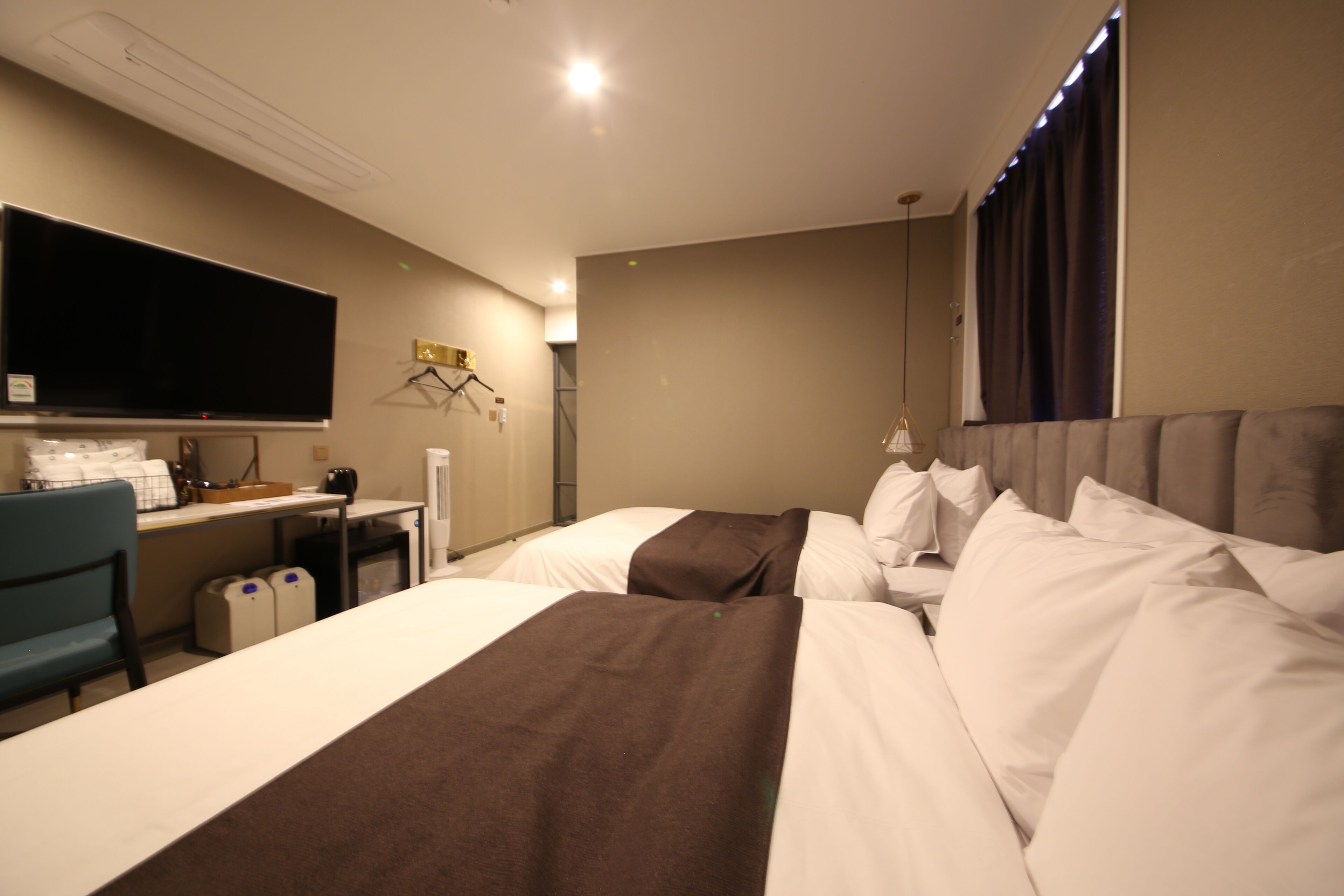A hotel room with two beds, a desk, a television, and a chair.