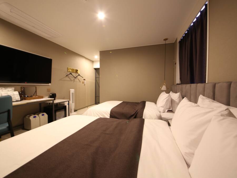 A hotel room with two beds, a desk, a television, and a chair.