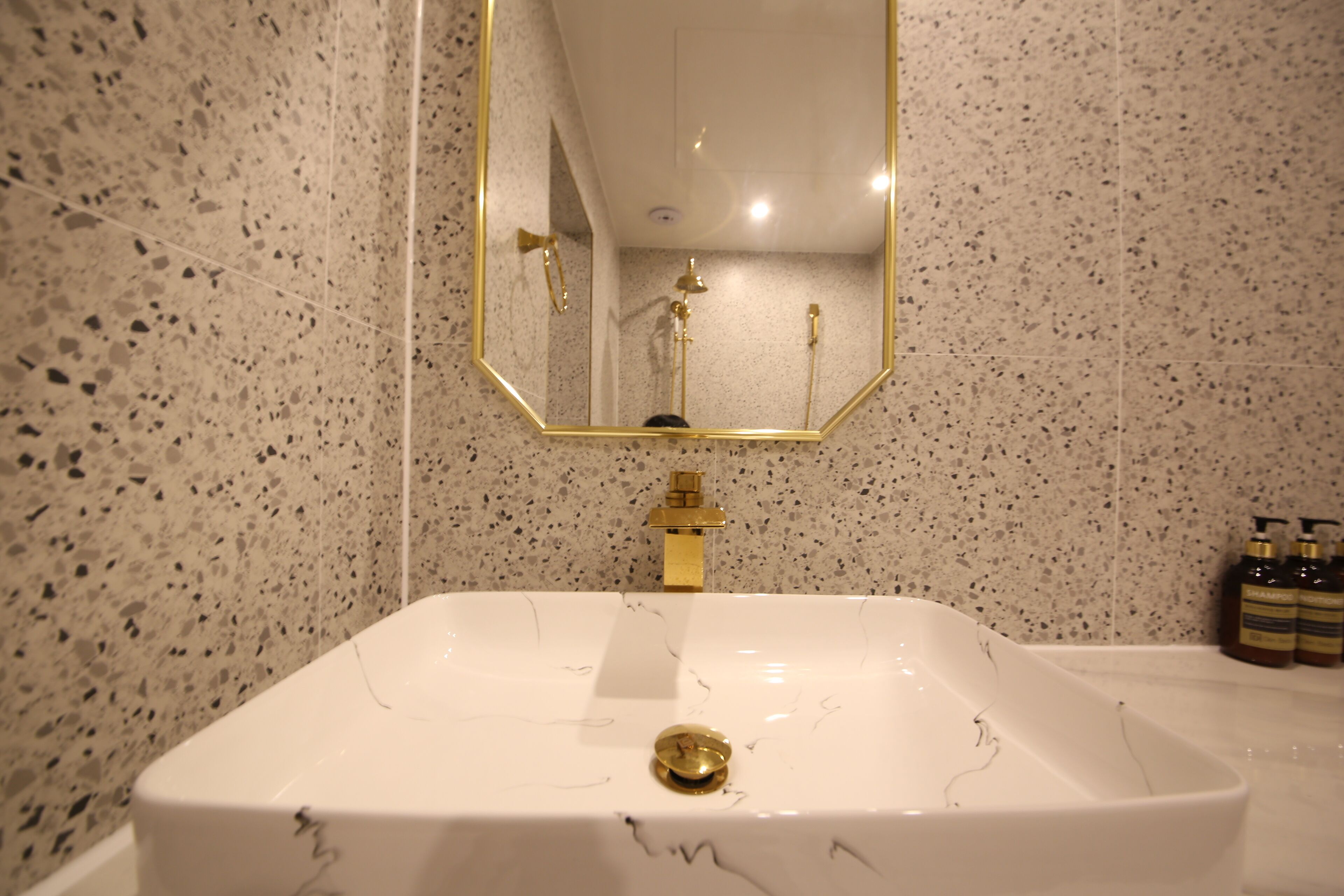Un baño con un lavamanos blanco, un grifo dorado y un espejo con marco dorado.
