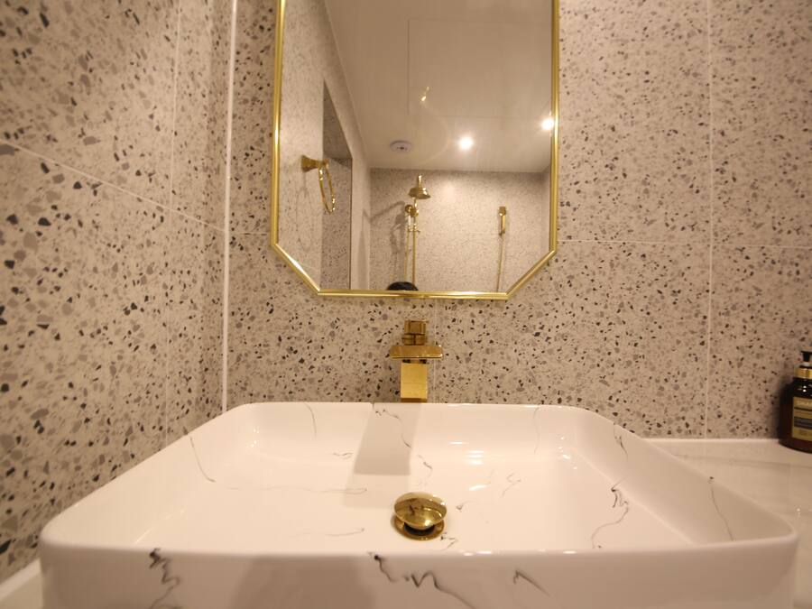 Un baño con un lavamanos blanco, un grifo dorado y un espejo con marco dorado.