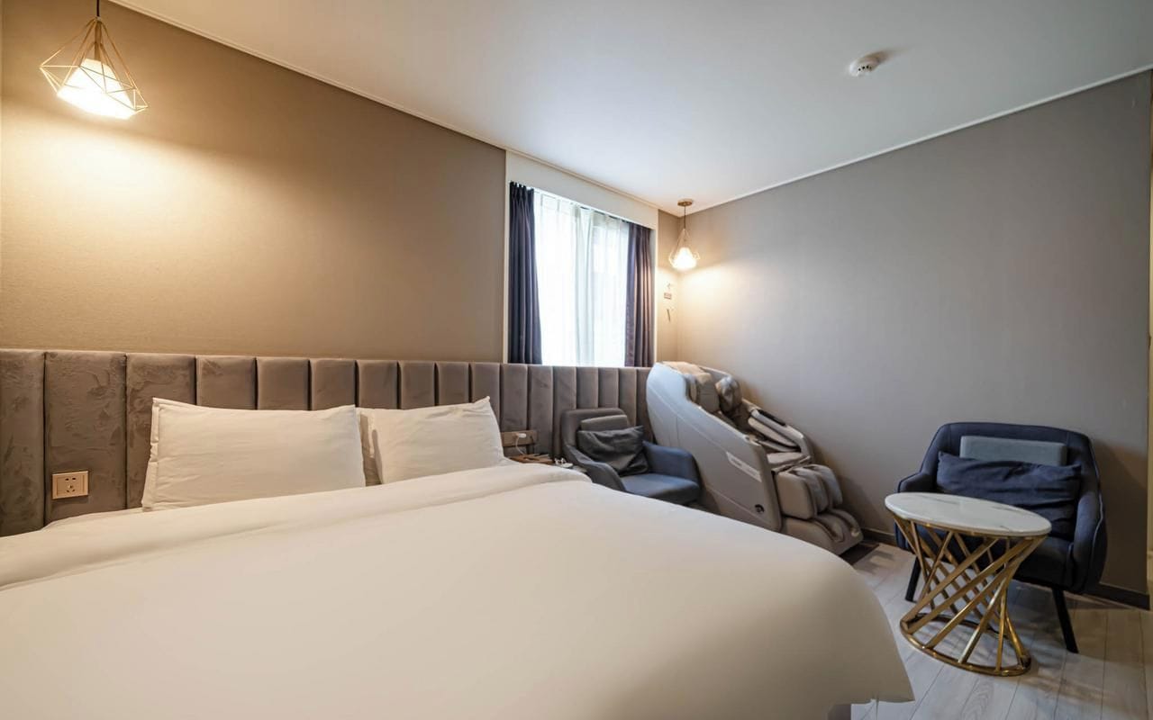 Una habitación de hotel con una cama grande, una zona de estar con sofá y sillones, y una mesita.