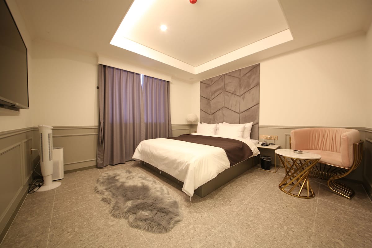 A modern hotel room with a large bed, a round gold table, and a fluffy rug.