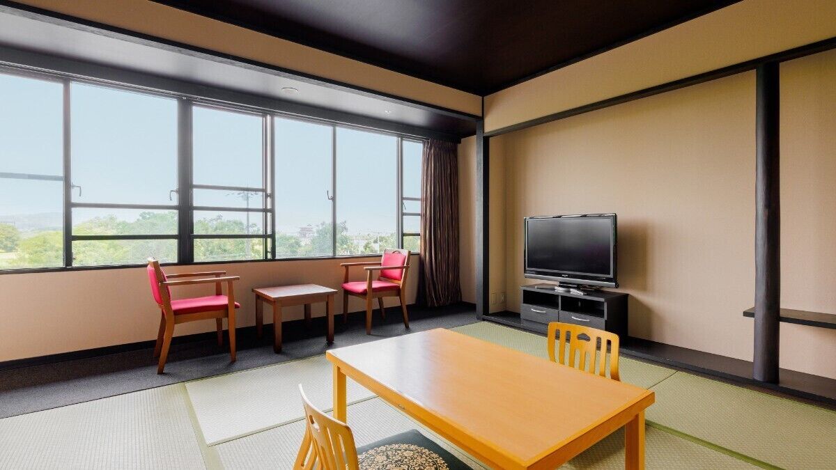 A room with tatami mats, a wooden table, two chairs, a TV, and large windows.
