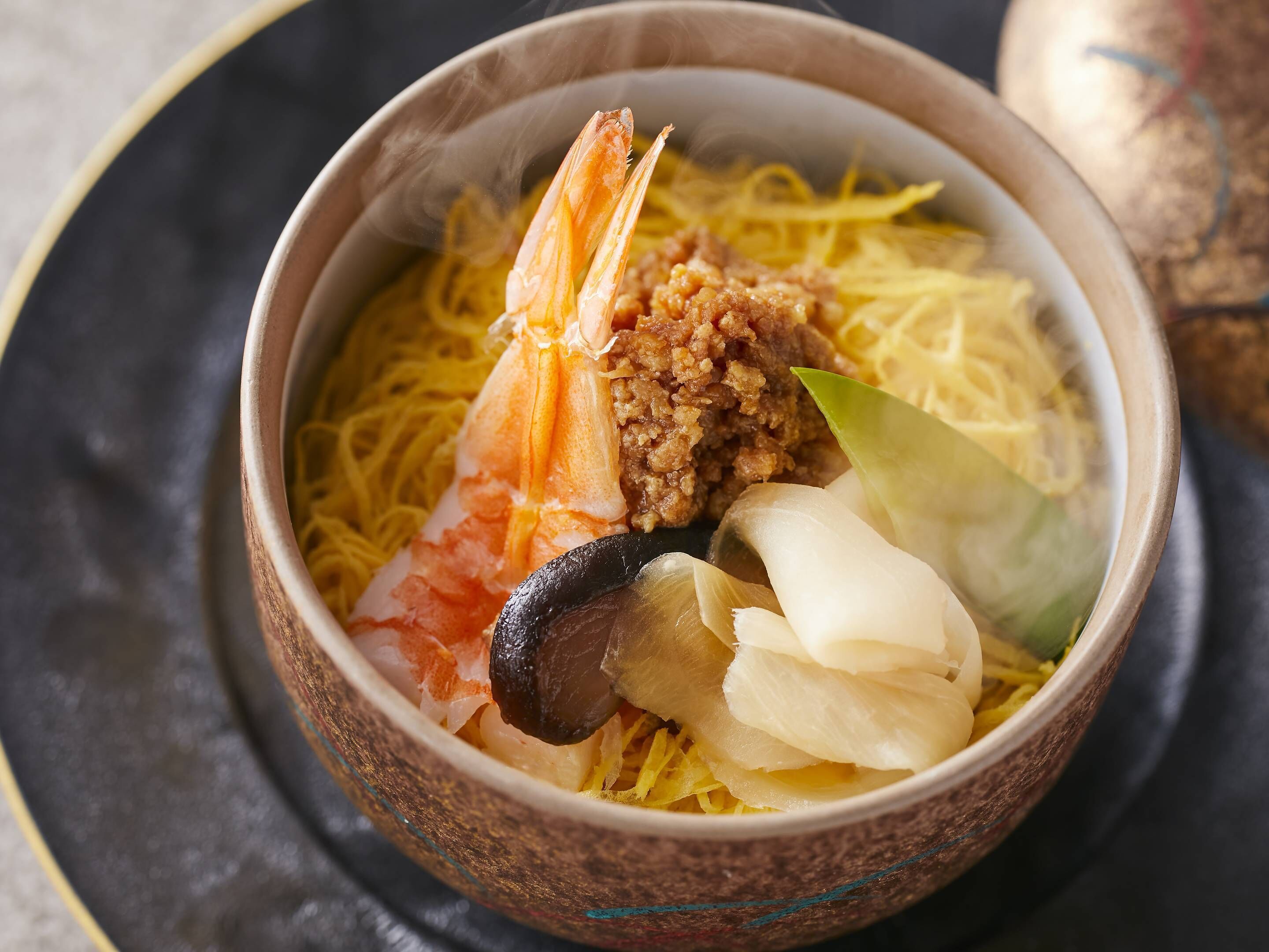 A bowl of food with noodles, shrimp, and other ingredients.