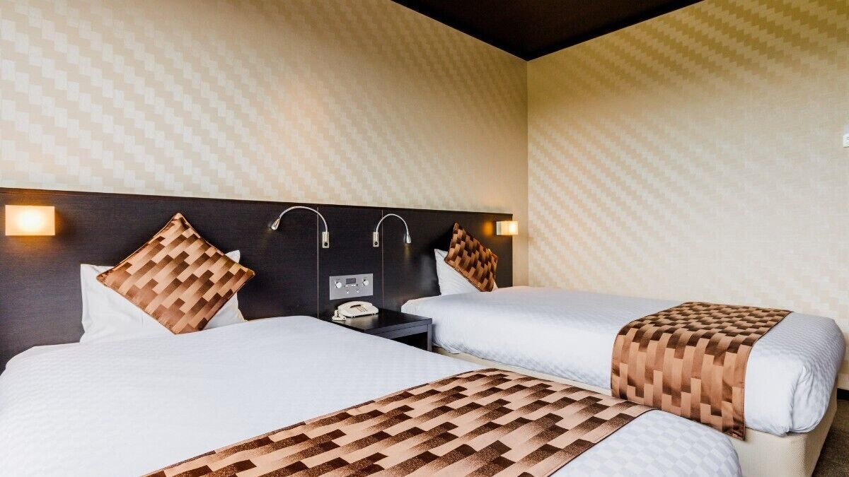 A hotel room with two beds, a nightstand, and wall-mounted lamps.