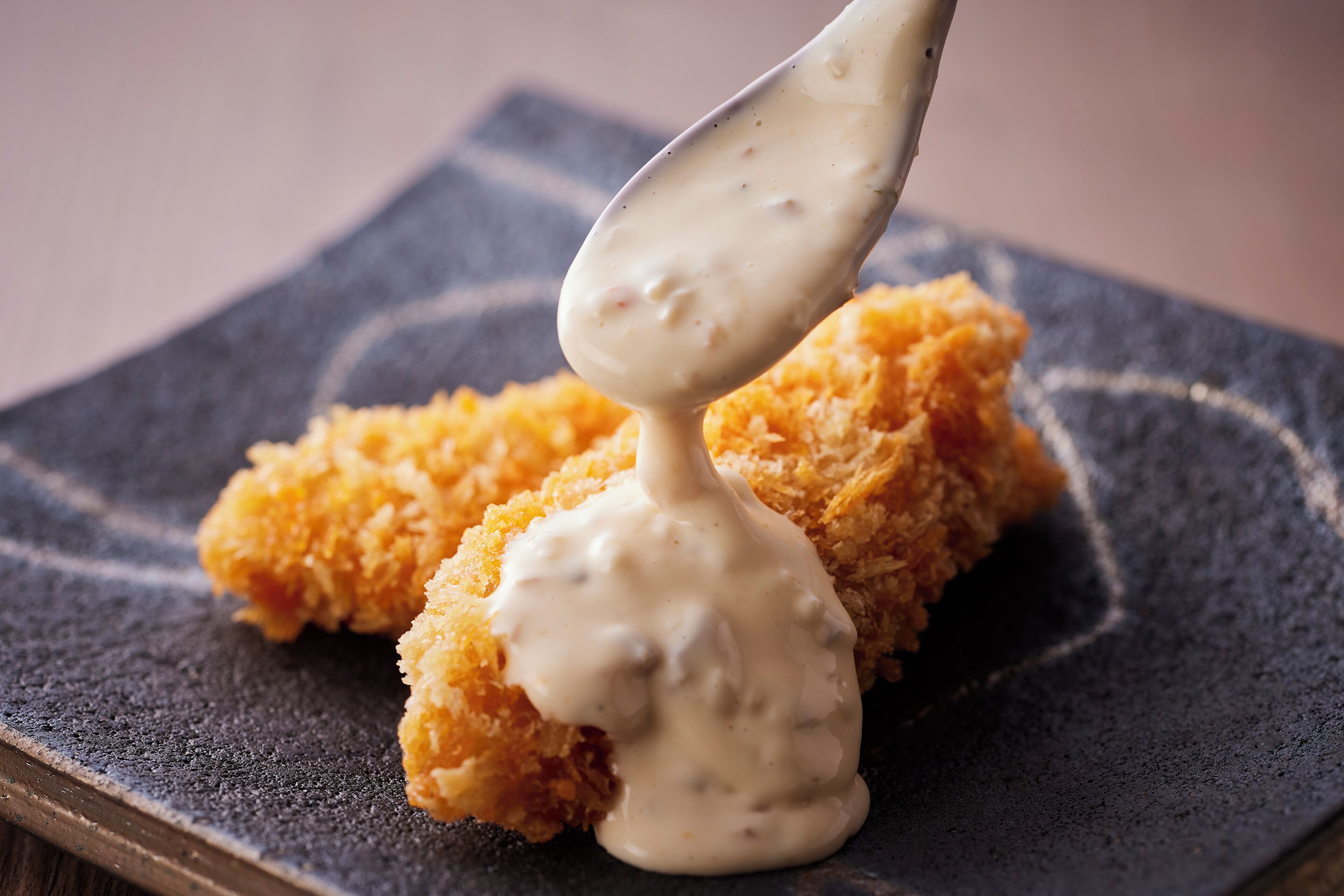 A spoonful of creamy sauce being lifted from a dish of breaded food.