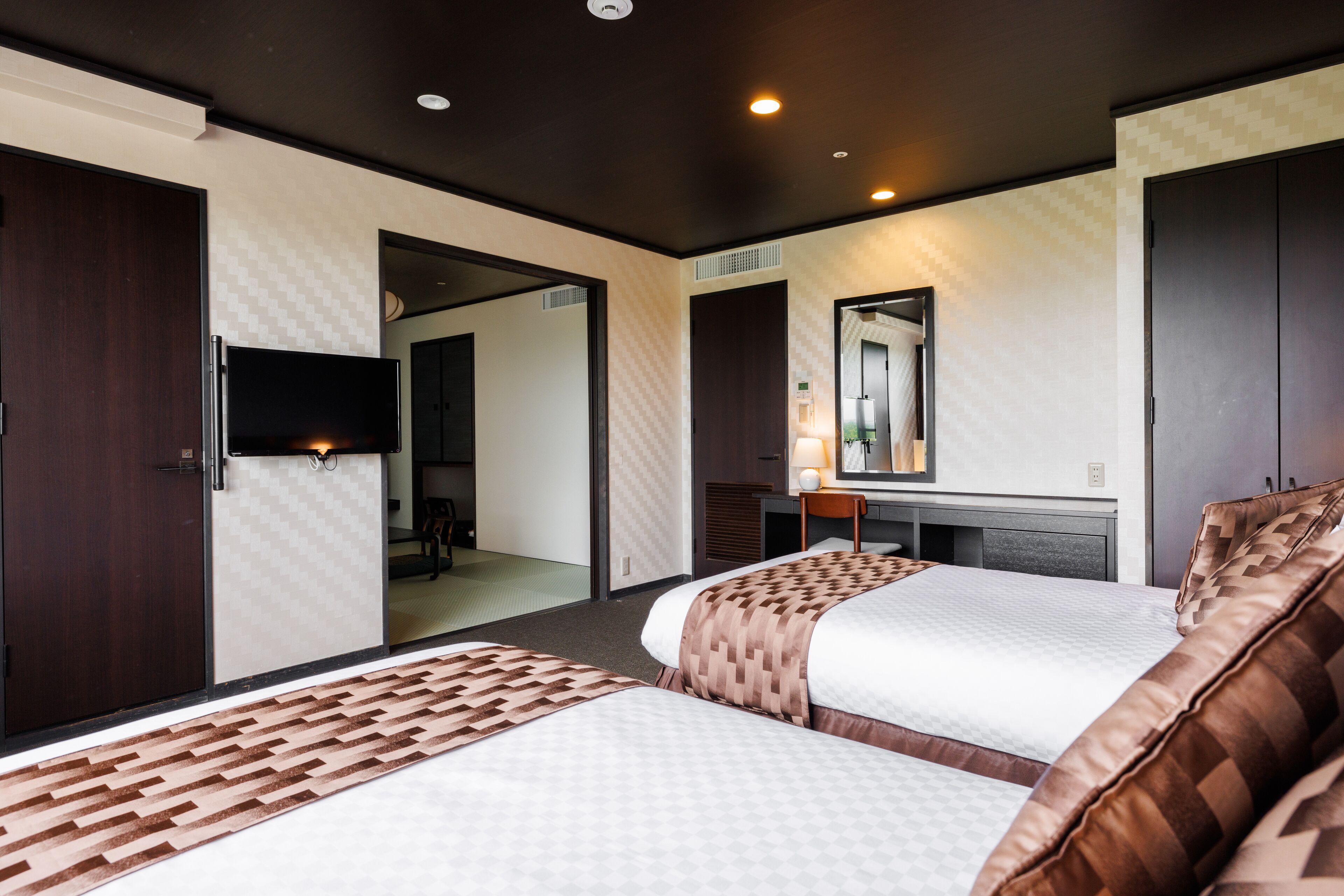 A hotel room with two beds, a TV, a desk, and a mirror.