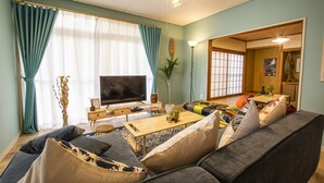 Un salon comprenant un canapé, un téléviseur, une table basse en bois et un coin repas avec une table et des chaises.