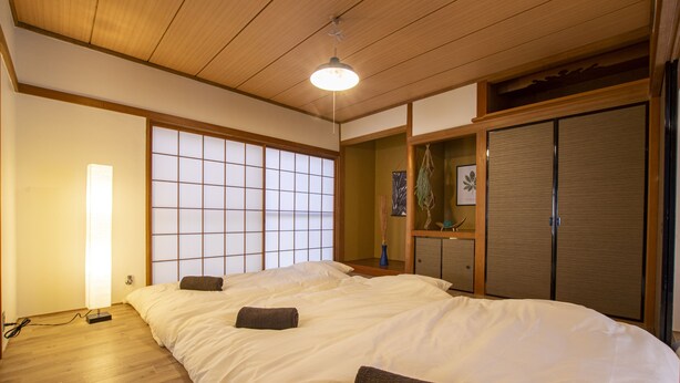 Une chambre de style japonais traditionnel, avec un sol recouvert de tatamis, un grand lit avec une literie blanche, un paravent shoji et une porte coulissante.