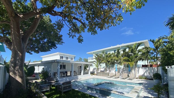Um quintal com piscina, uma árvore e uma casa branca.
