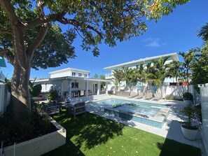 A backyard with a swimming pool, a tree, and a white house.