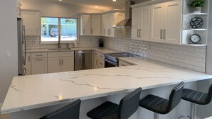 Uma cozinha moderna com armários brancos, bancada de mármore e um espaço bar embutido com banquetas pretas.