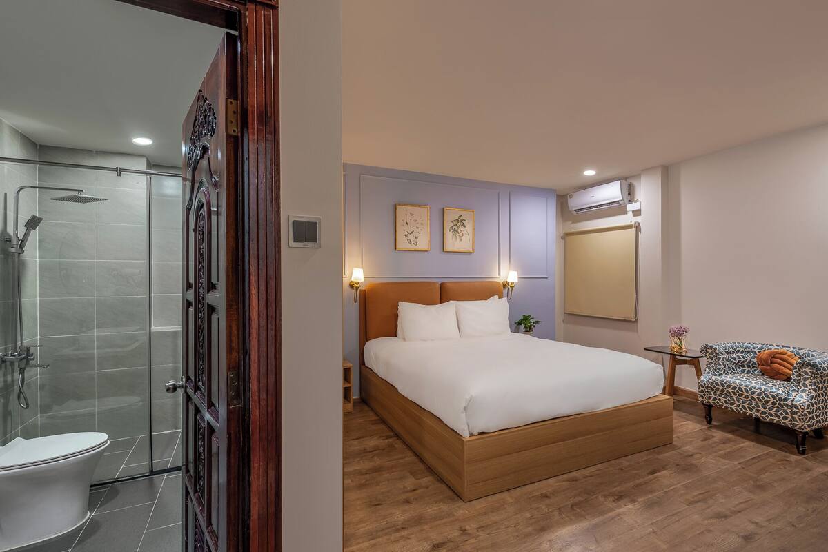 Une chambre avec un lit en bois, une cabine de douche en verre et une petite table de chevet avec une lampe.