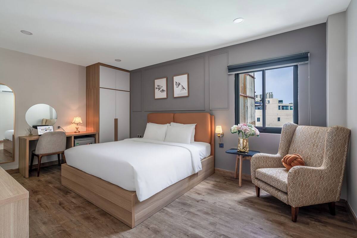Une chambre d’hôtel moderne, dotée d’un grand lit, d’un bureau, d’une chaise et d’une fenêtre donnant sur la ville.