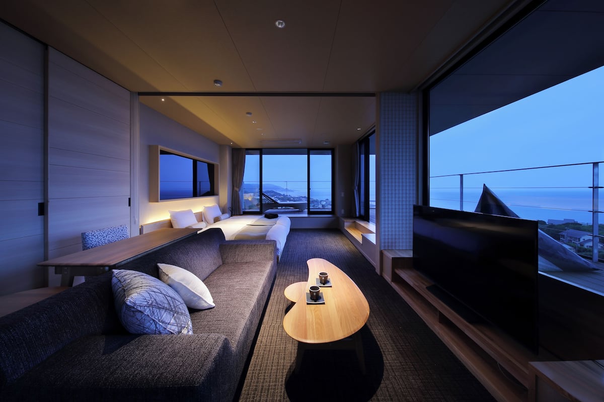 A modern hotel room with a large TV, a sofa, a coffee table, and a view of the city.