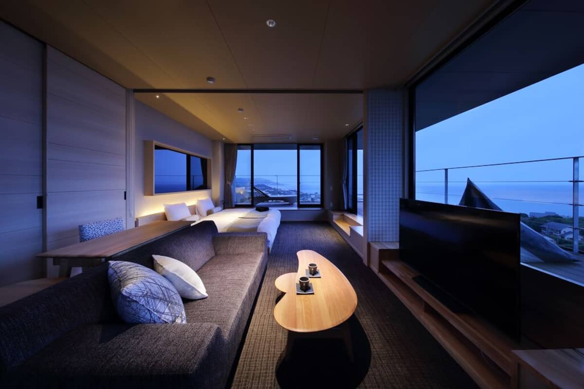 A modern hotel room with a large TV, a sofa, a coffee table, and a view of the cityscape.