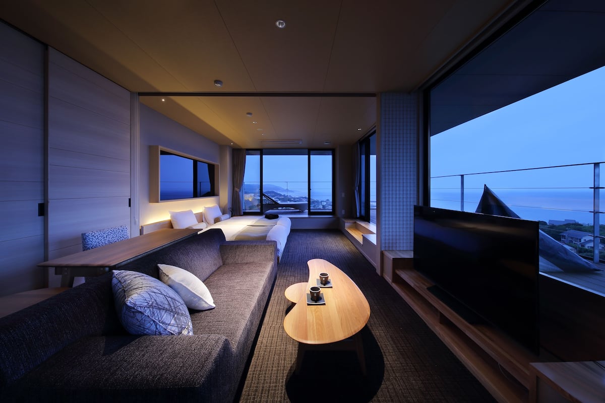 A modern hotel room with a large TV, a sofa, a coffee table, and a view of the city.