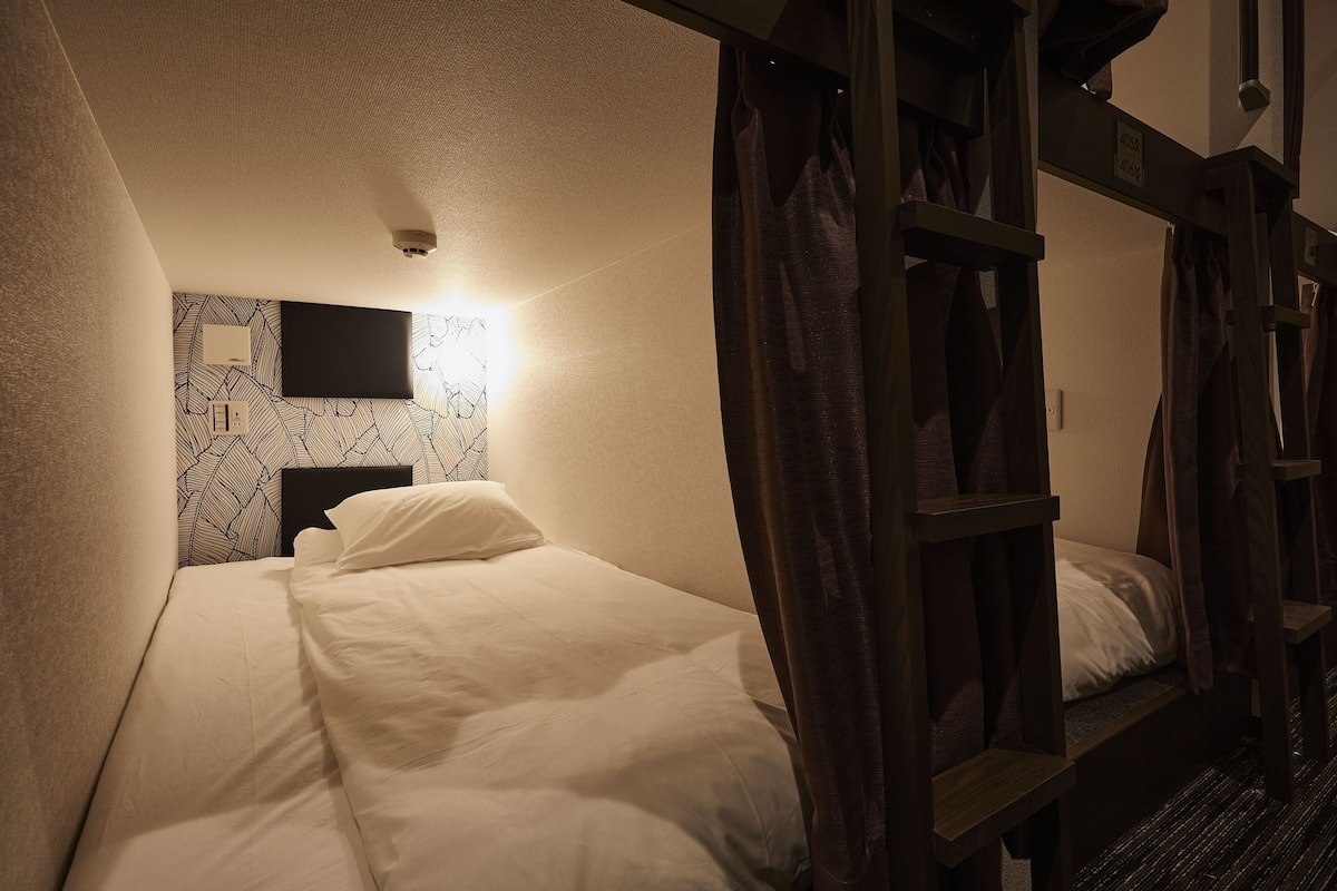 Una cama individual con cabecera, un televisor de pantalla plana montado en la pared y un papel tapiz estampado.