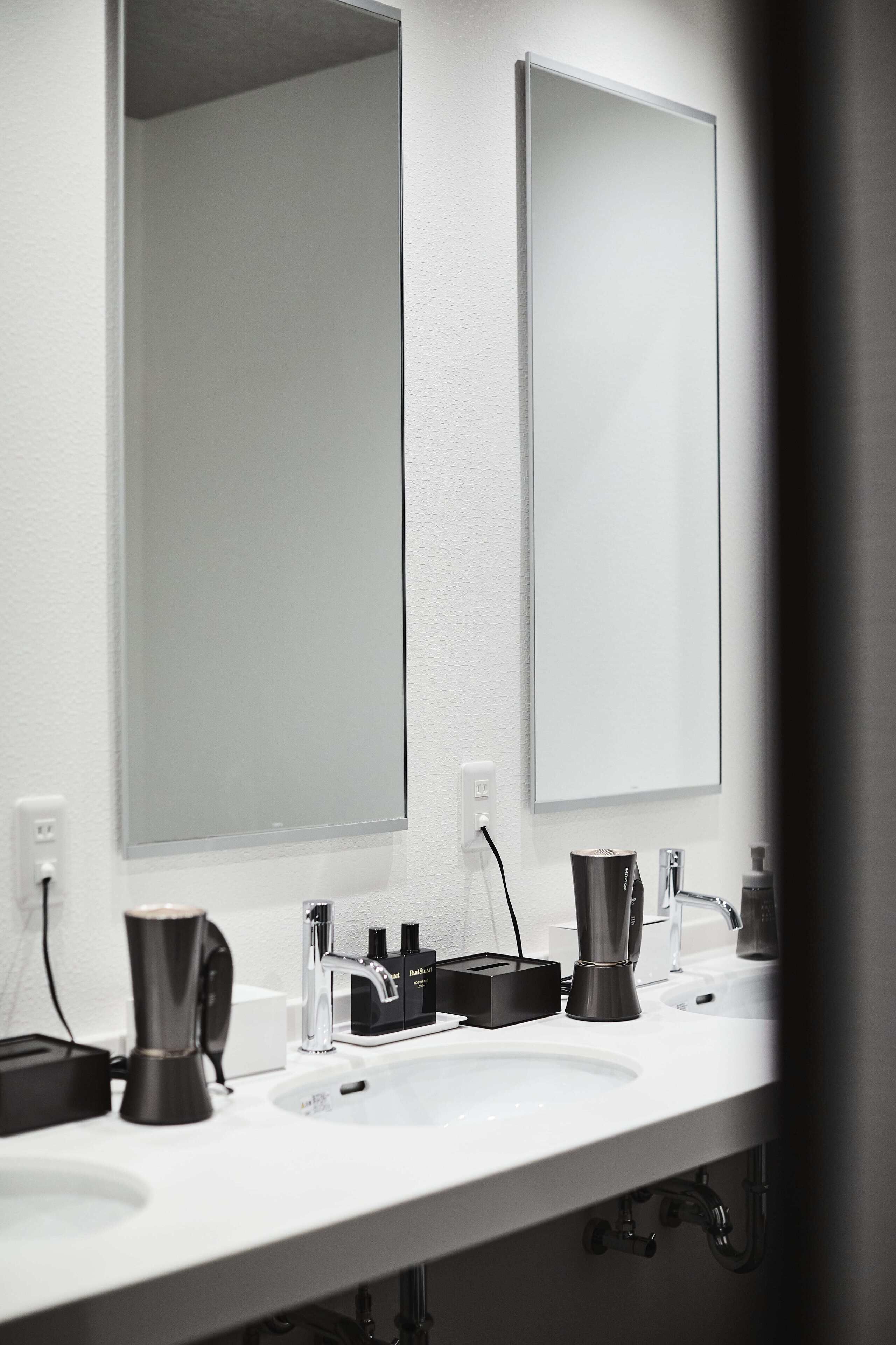 A modern bathroom with a white sink, two mirrors, and a coffee maker.
