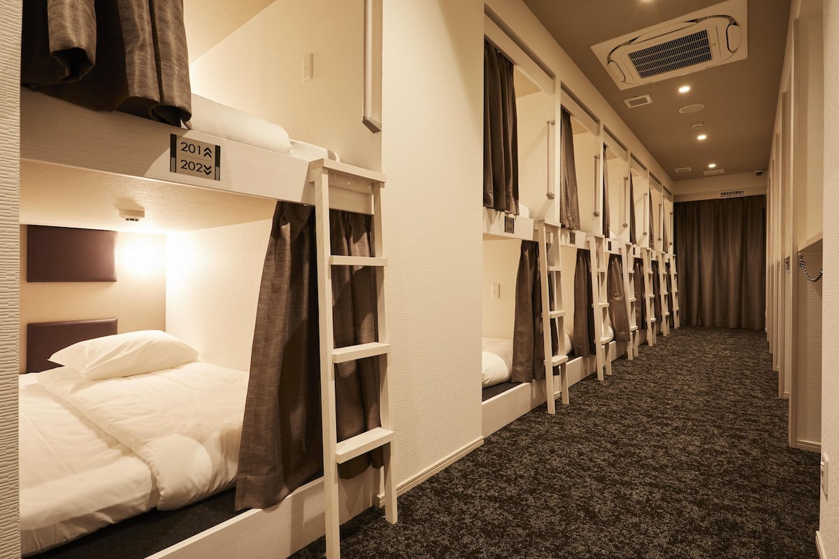 Una habitación de hotel con literas, piso alfombrado y un respiradero en el techo.