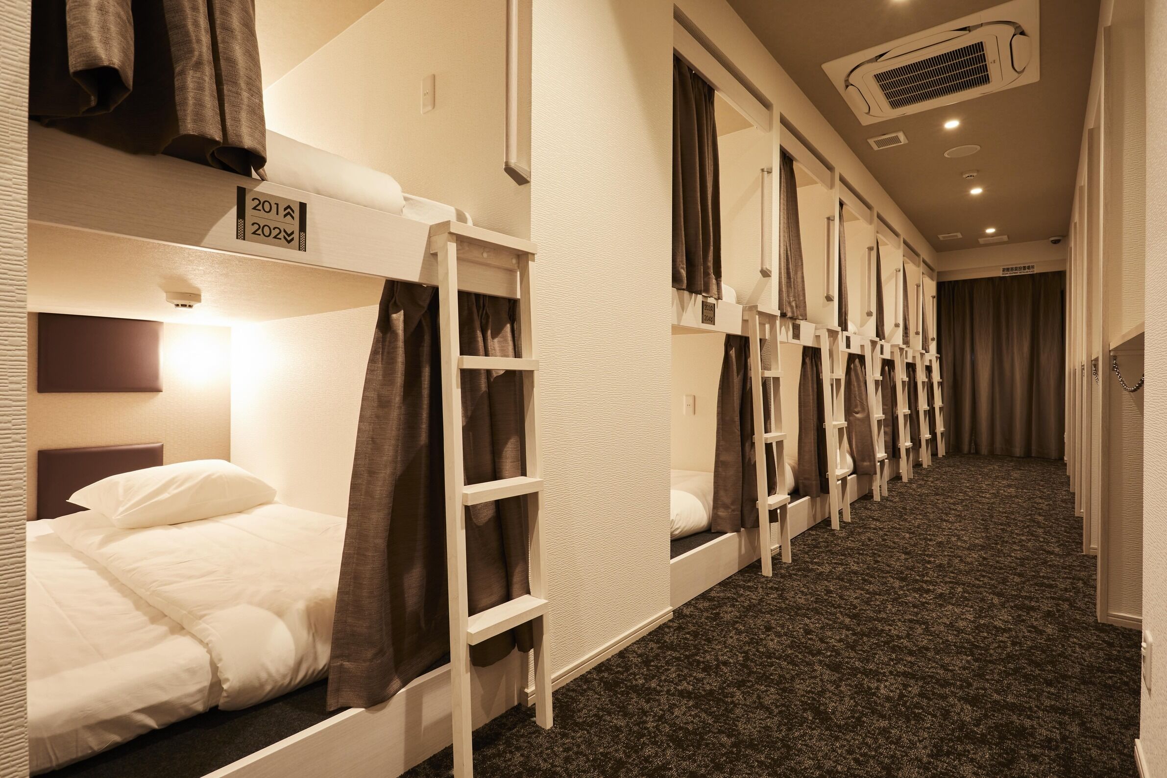 Ein Hotelzimmer mit Etagenbetten, Teppichboden und einer sichtbaren Klimaanlage.
