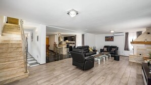 A spacious living area with a modern design, featuring a black leather sofa, a dining table, and a kitchen area in the background.