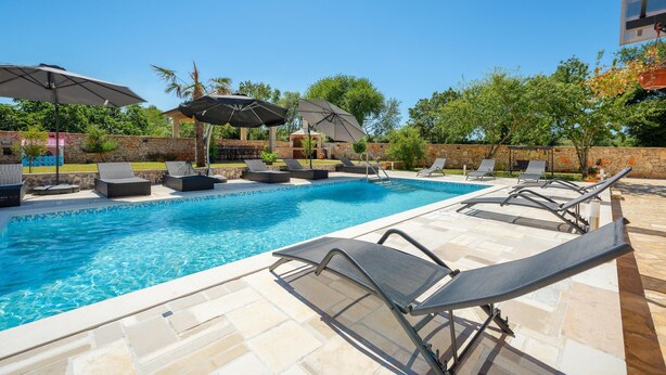 A swimming pool with lounge chairs and umbrellas, surrounded by stone walls and greenery.