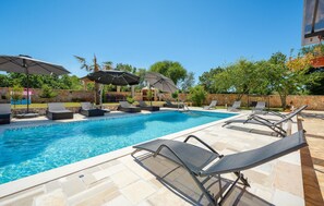 Ein Pool mit Liegestühlen und Sonnenschirmen, umgeben von Steinmauern und Grünflächen.