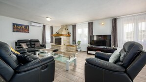 A modern living room with leather sofas, a glass coffee table, a fireplace, and a flat-screen TV.