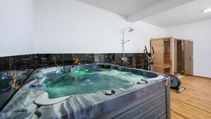 A modern bathroom with a large, rectangular hot tub, a shower area, and a wooden cabinet.
