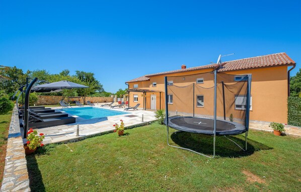 Ein Garten mit Schwimmbad, Trampolin und überdachter Terrasse.