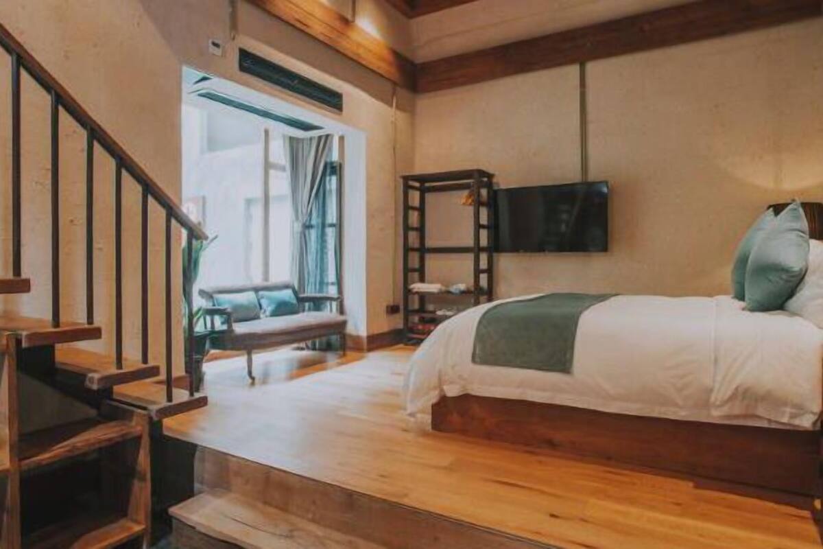 A bedroom with a wooden bed, a TV mounted on the wall, and a staircase leading to another room.