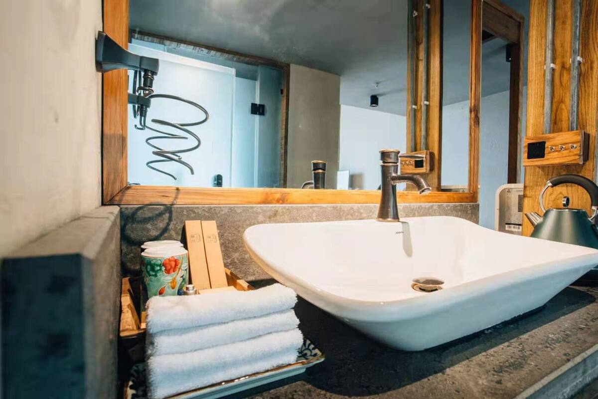 A bathroom with a white sink, wooden countertop, and a large mirror.