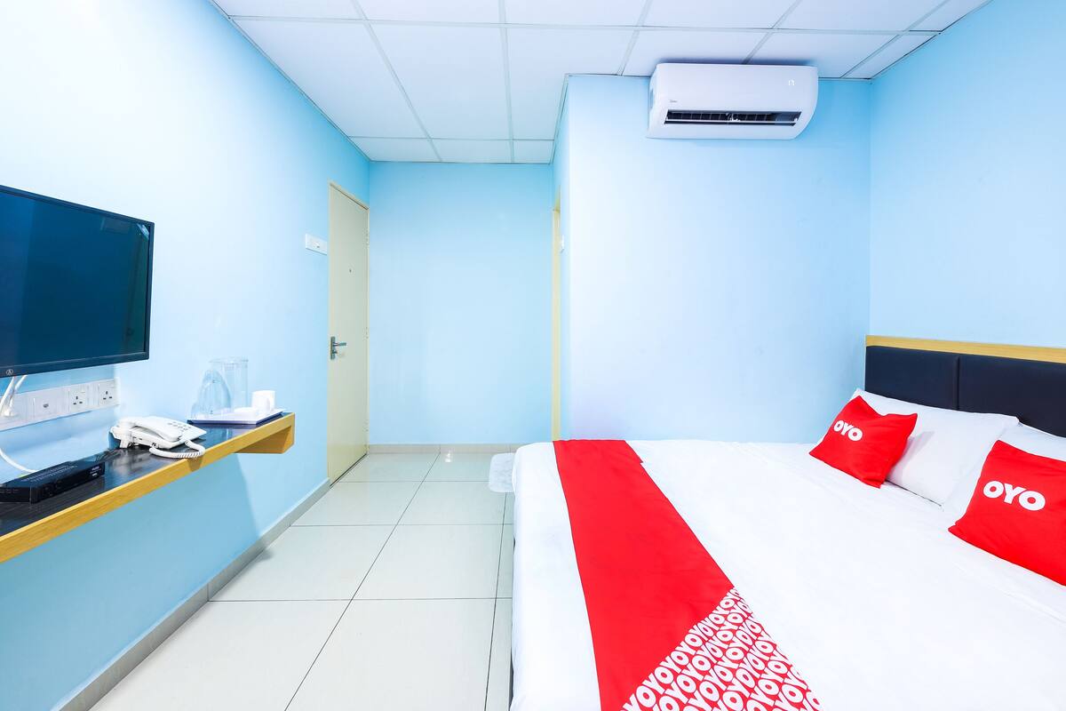 A hotel room with a bed, a desk with a computer, a phone, and an air conditioner.