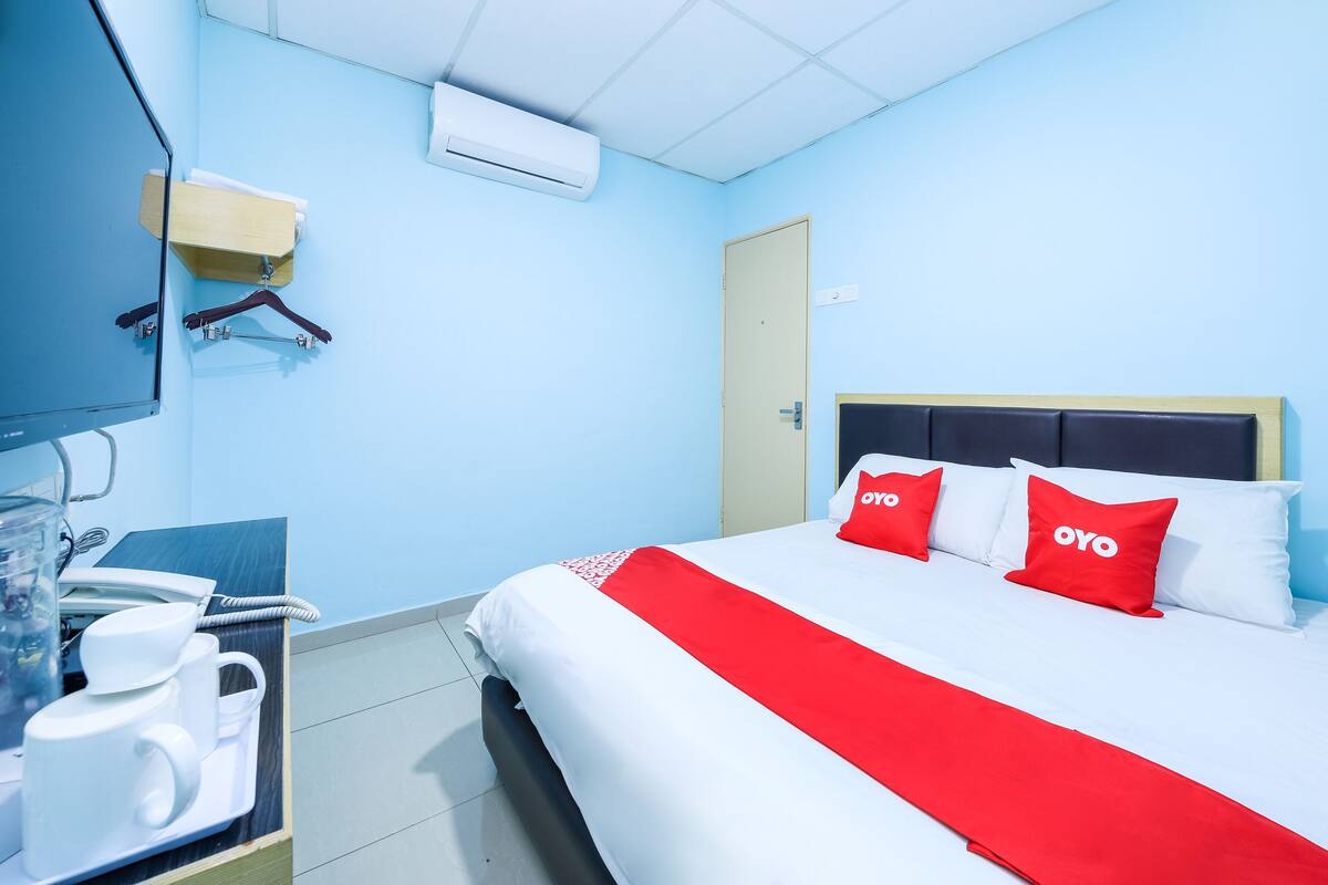 A hotel room with a bed, a TV, a desk with a phone, and a wall-mounted air conditioner.