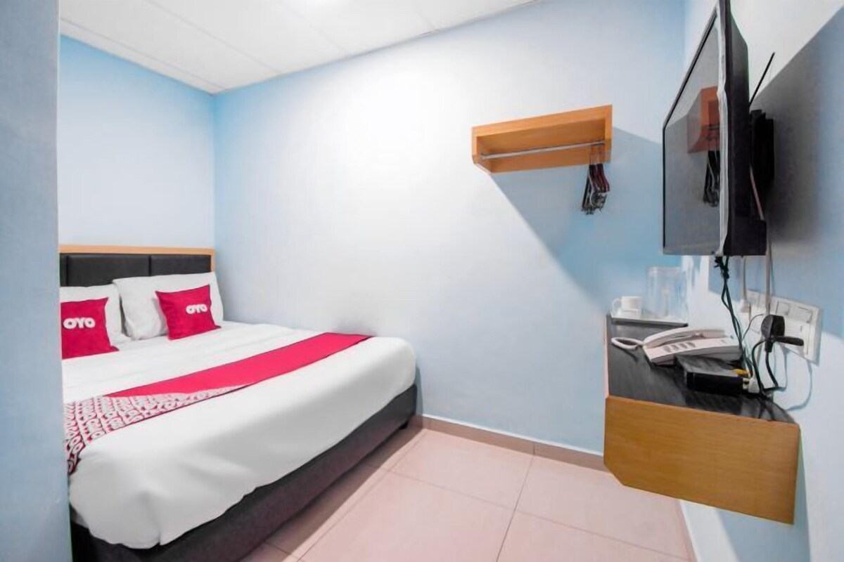 Ein Hotelzimmer mit einem Bett, einem Schreibtisch mit Telefon und einem an der Wand befestigten Fernseher.