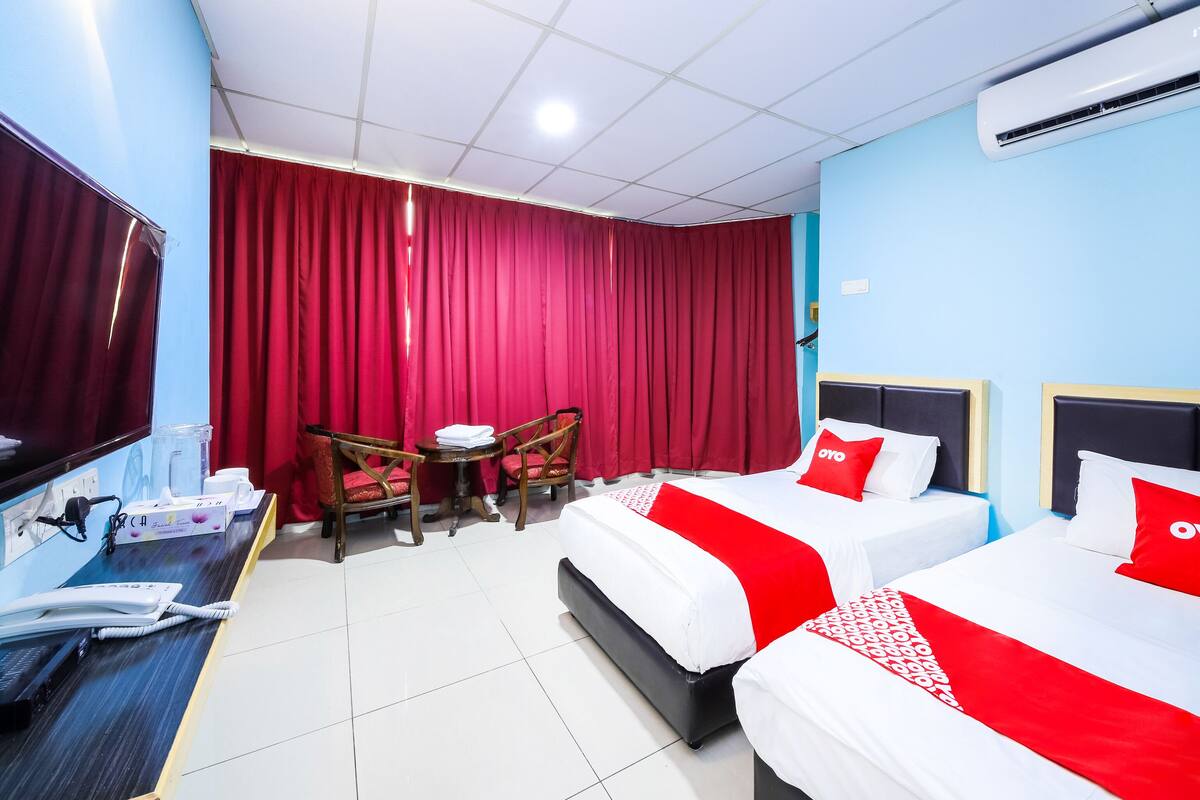 A hotel room with two beds, a desk, a TV, and a red curtain.