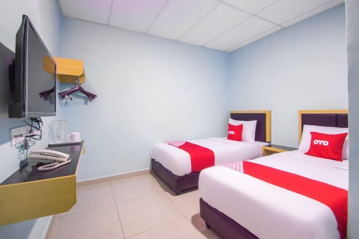 Ein Hotelzimmer mit zwei Betten, einem Fernseher, einem Schreibtisch mit Telefon und einem Spiegel.