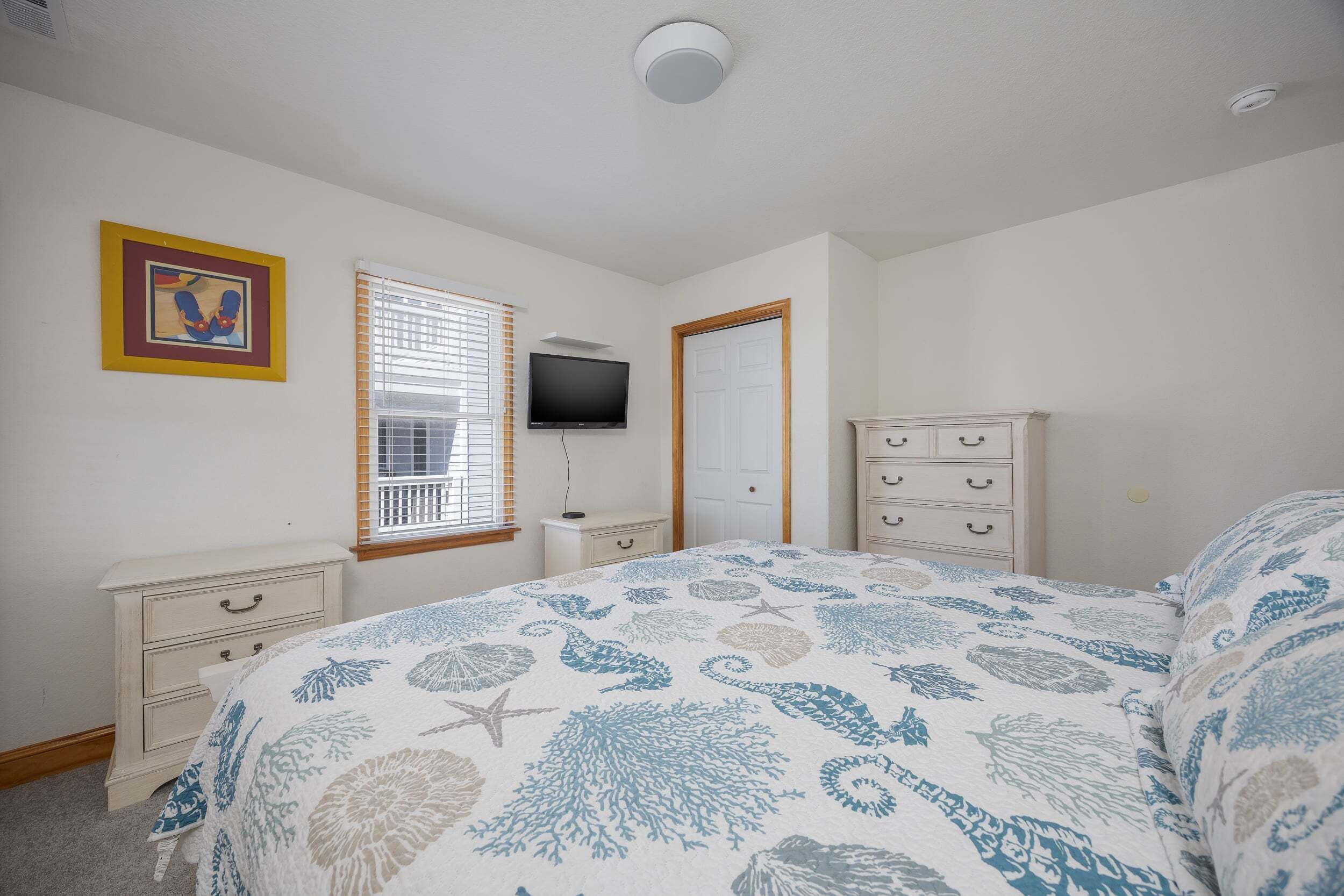 A bedroom with a bed, a dresser, a television, and a window with blinds.