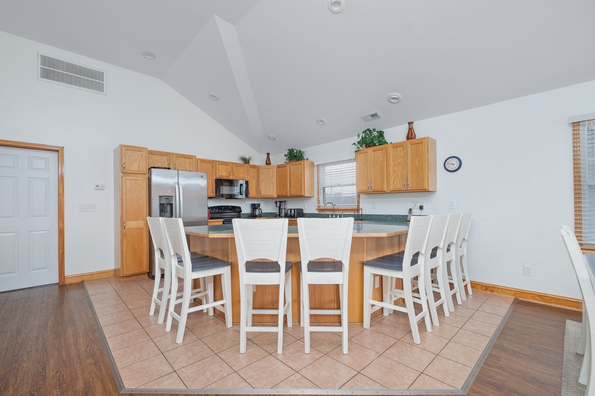 A modern kitchen with a central island, wooden cabinets, and a dining area with white chairs.