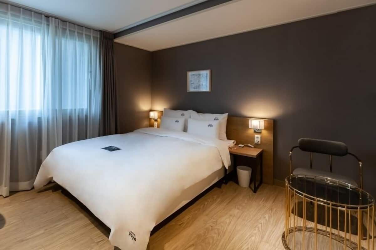 A hotel room with a large bed, two bedside tables with lamps, a chair, and a small table.