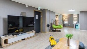 A modern living room with a flat-screen TV, a hanging chair, a small toy car, and a wooden coffee table. - YAJA Hotel Tongyeong Ferry Terminal Branch (Tongyeong)